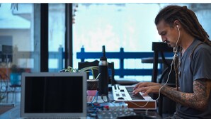 Eine Person spielt Keyboard, auf dem Tisch befinden sich ein Laptop und diverses elektronisches Equipment.