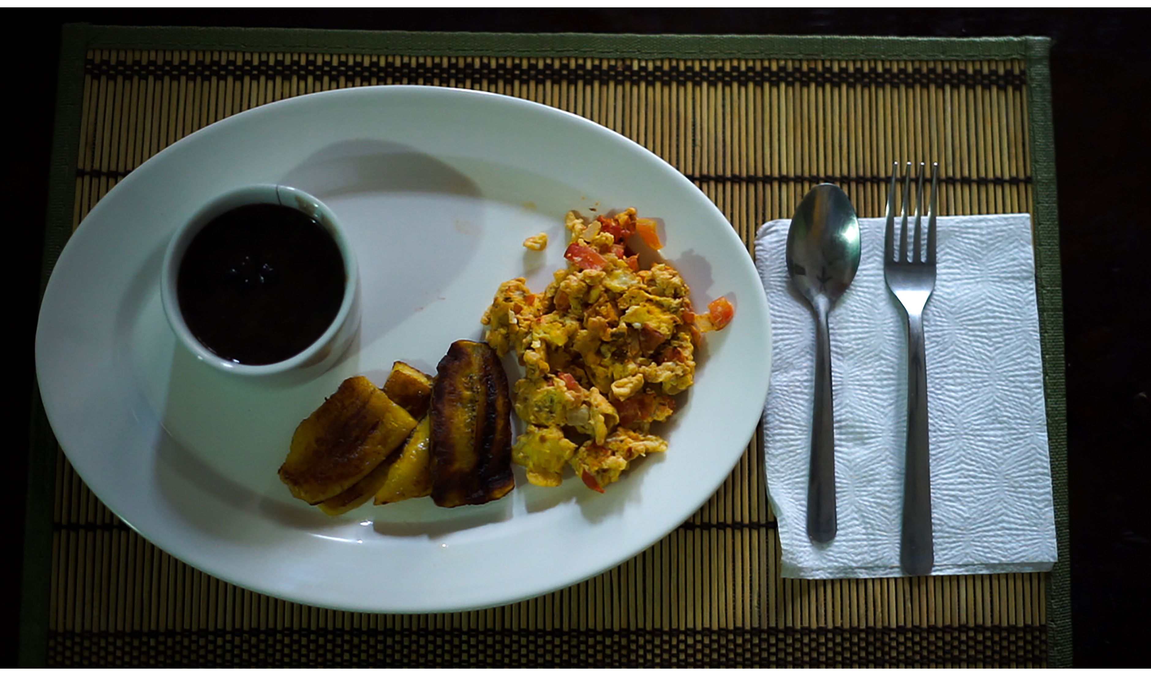 Un plato con huevos revueltos, tostadas y una taza de café negro sobre una estera de bambú.