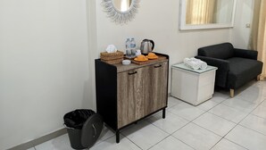 A compact room with a wooden cabinet, a small white table, a black trash bin, a dark sofa, and a large mirror on the wall. - Fastrooms Bekasi Hotel (Bekasi)