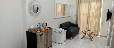 Una habitación limpia y moderna con un armario de madera, un sofá negro, una mesa de vidrio y un espejo en la pared.