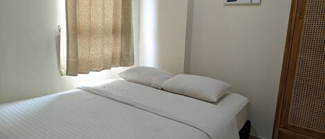 A bedroom with a bed, a window with curtains, a wall-mounted artwork, and a wooden wardrobe.