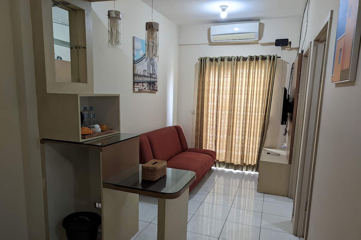 A compact living space with a sofa, a small table, a trash bin, and an air conditioning unit.