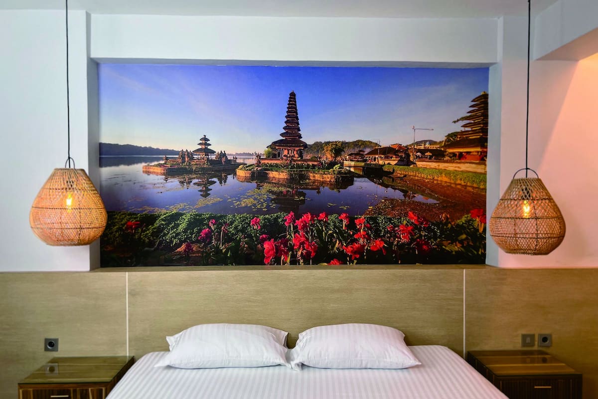 A bedroom with a large wall mural of a temple and lotus pond, two wicker lamps, and a neatly made bed with white pillows.