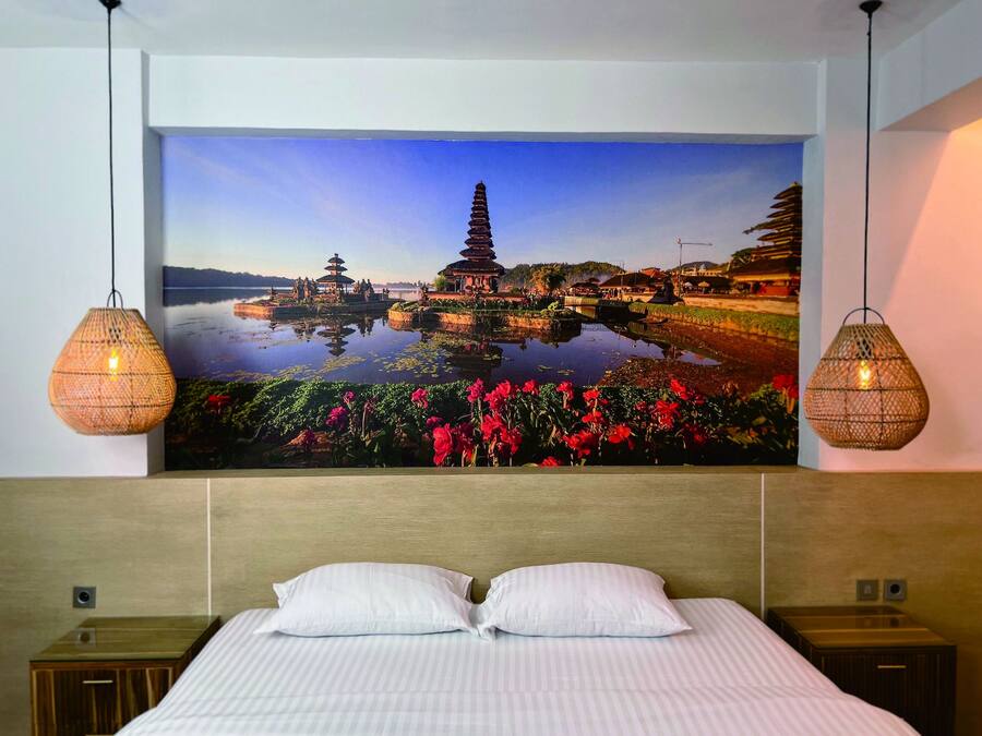 A bedroom with a large wall mural of a temple and lotus pond, two wicker lamps, and a neatly made bed with white pillows.