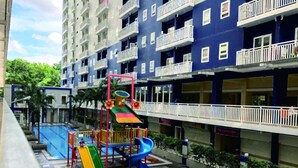 A playground with slides and a climbing structure, surrounded by a pool and a blue patterned floor. - Fastrooms Bekasi Hotel (Bekasi)