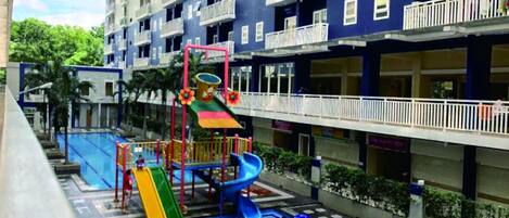A playground with slides and a climbing structure, surrounded by a pool and a blue patterned floor.