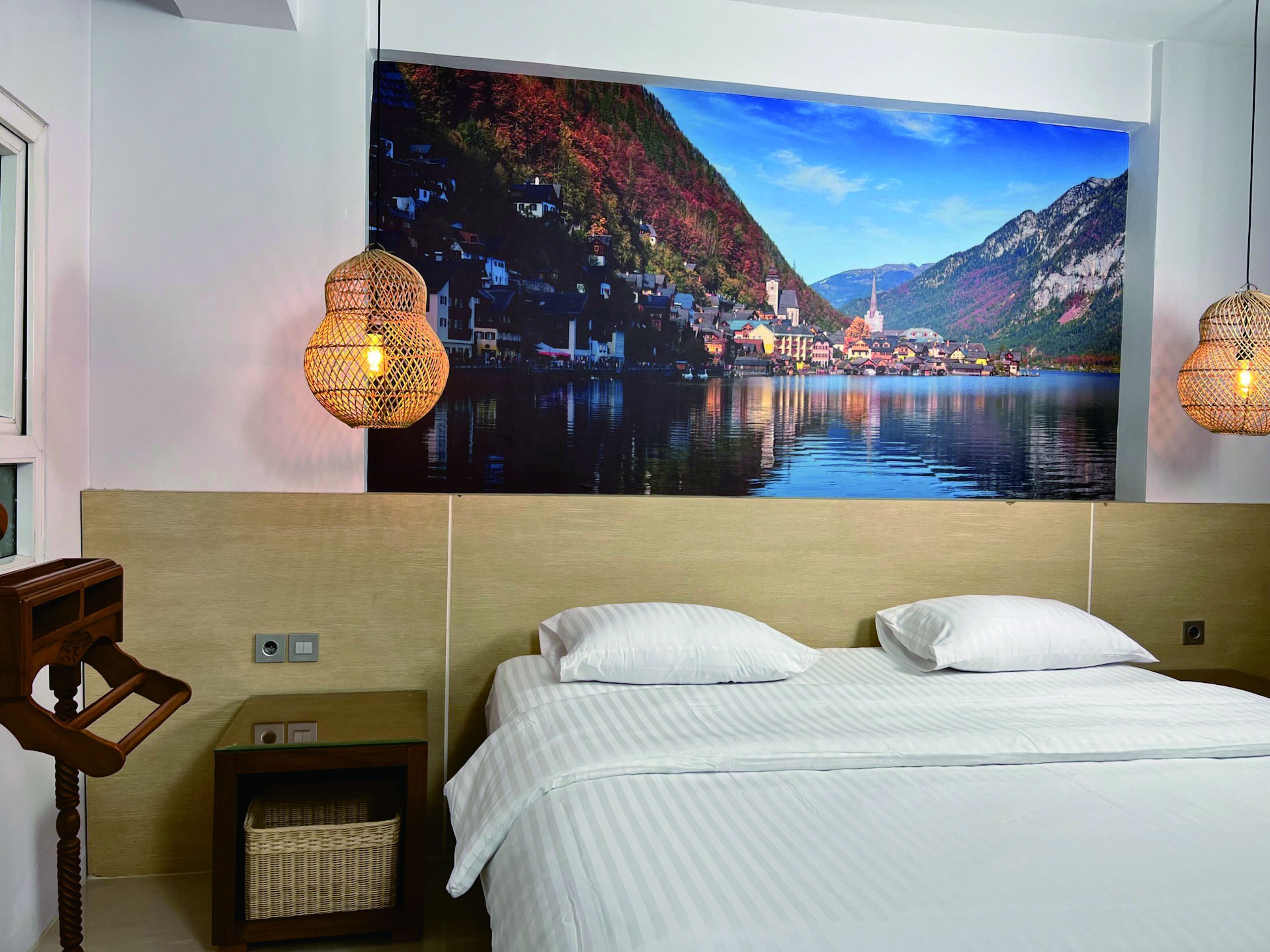 Quarto de hotel com uma cama, duas luminárias fixadas na parede, uma mesa de cabeceira e um grande mural com paisagem.