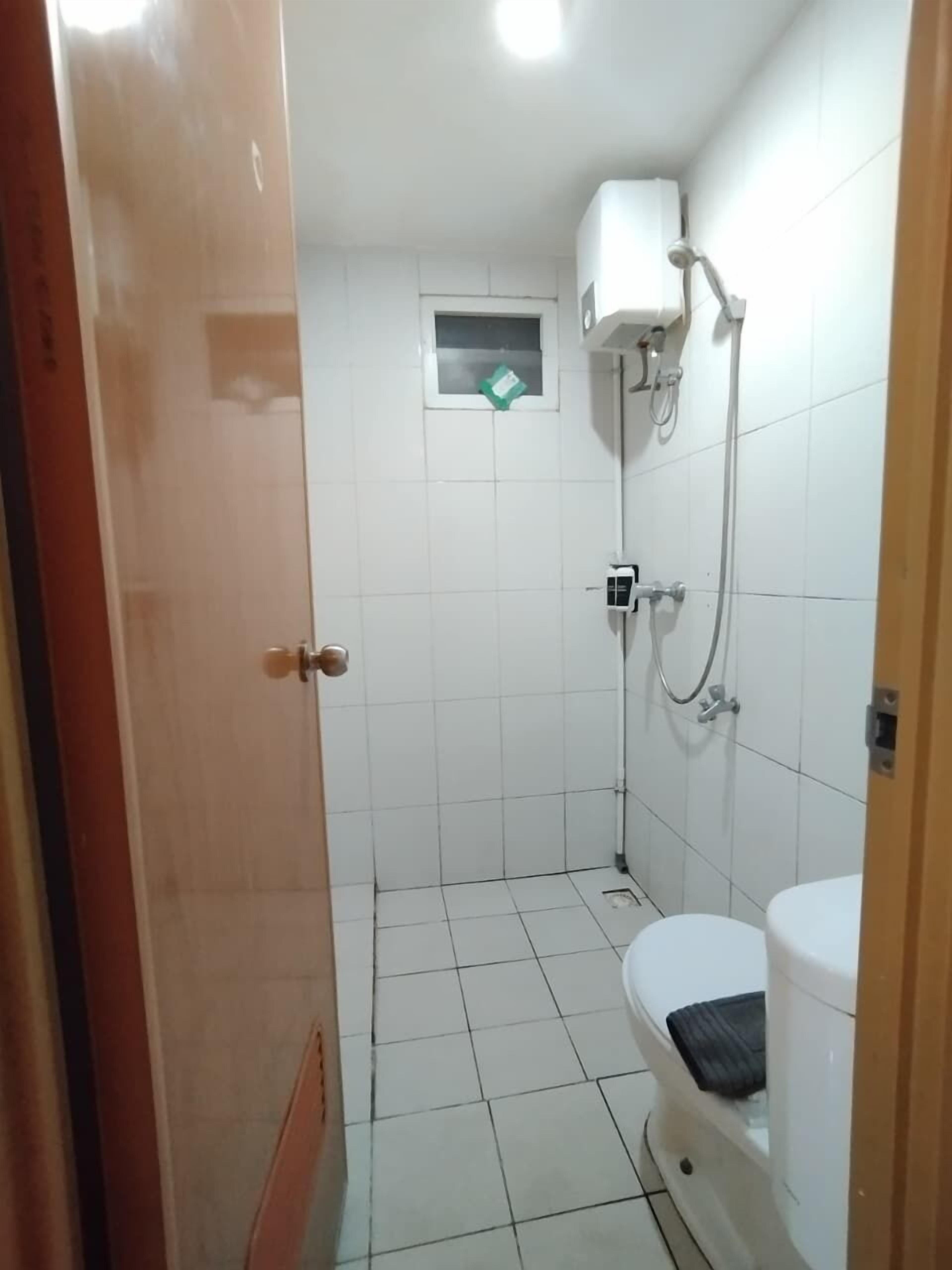 A small, tiled bathroom with a toilet, a shower area, and a window.