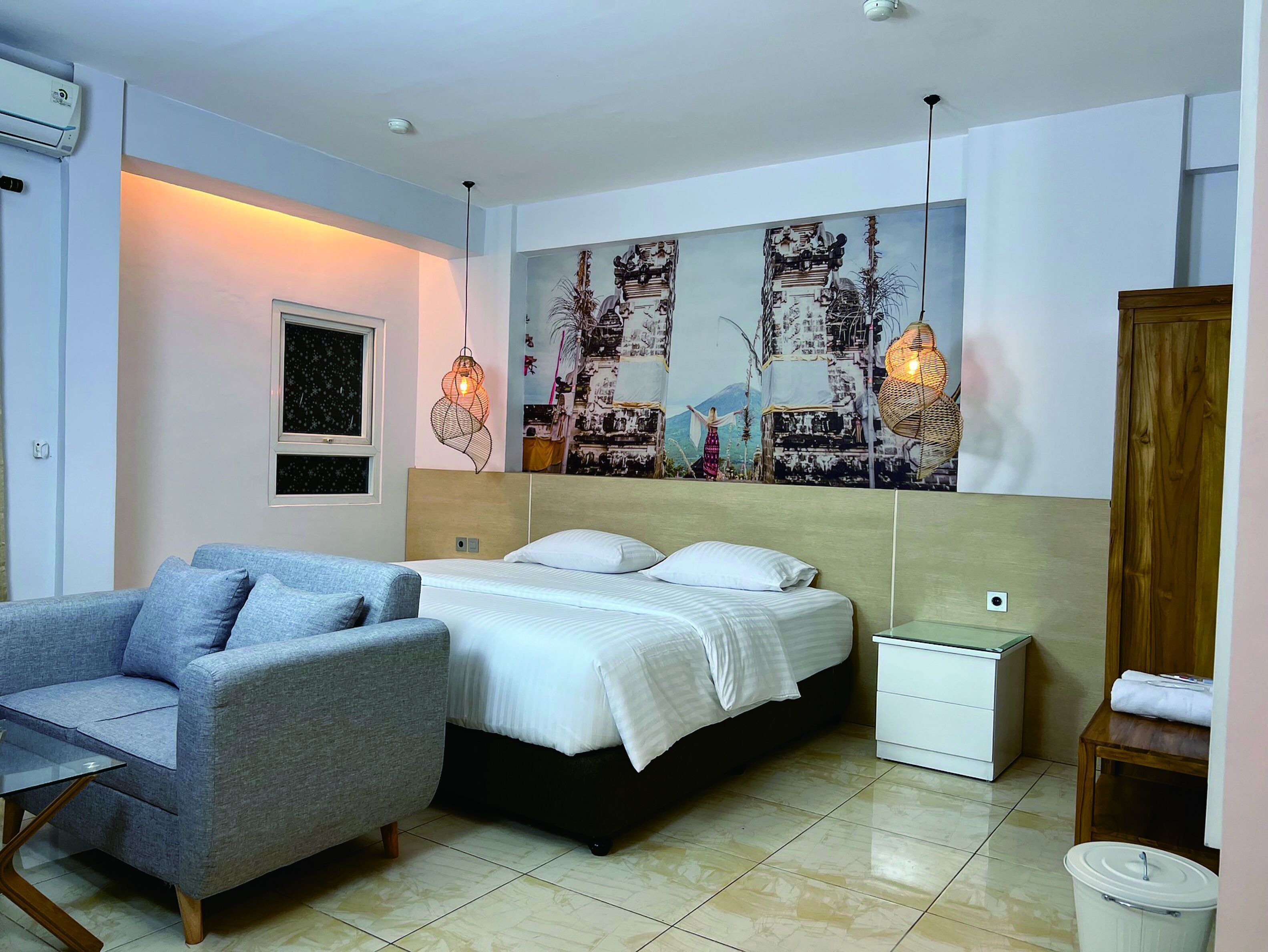 Une chambre à coucher comprenant un lit, un canapé gris, une table de chevet, un climatiseur fixé au mur et une grande fresque murale.