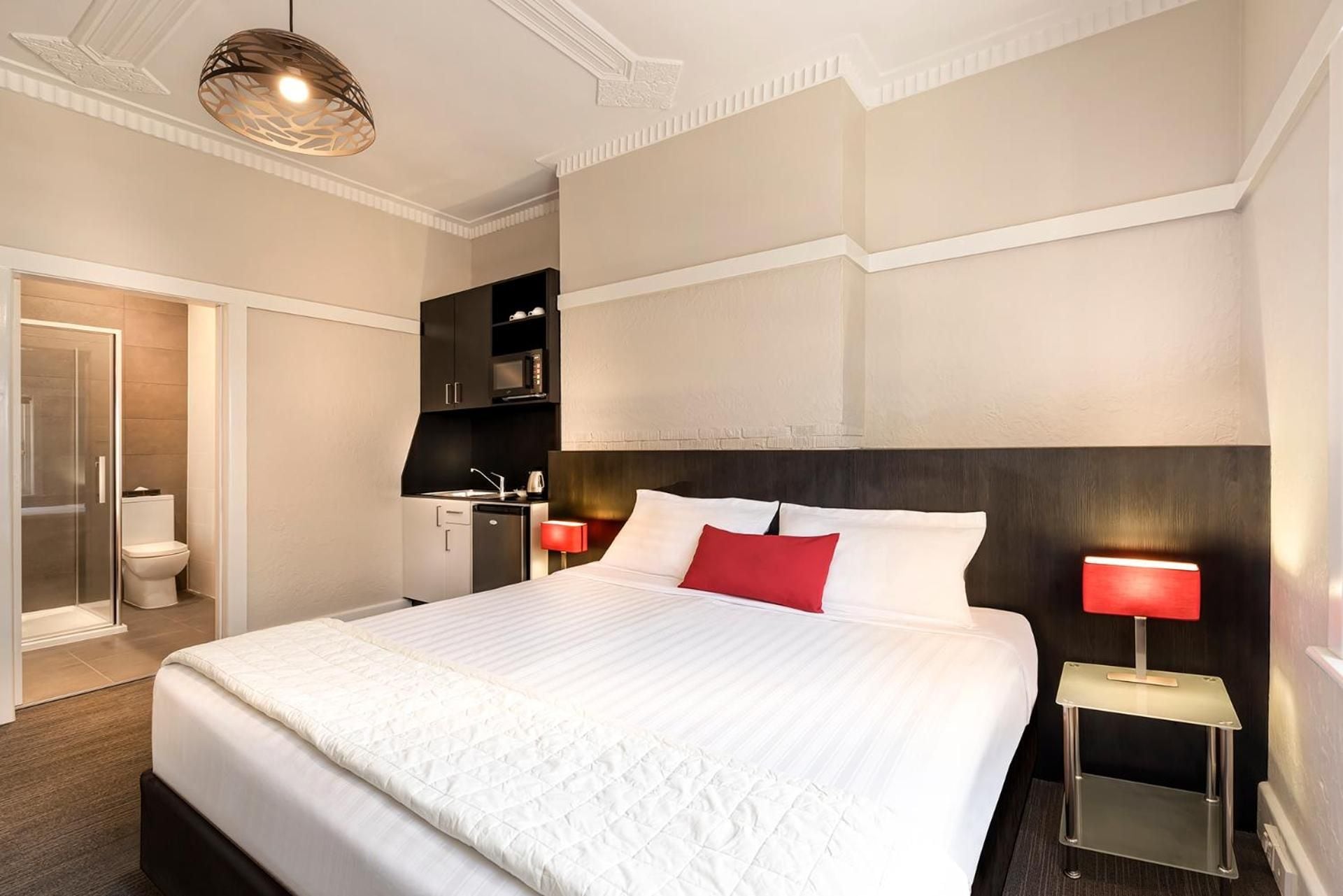 Ein Hotelzimmer mit einem großen Bett, einem Nachttisch mit Lampe, einem Kleiderschrank und einem Duschbereich.