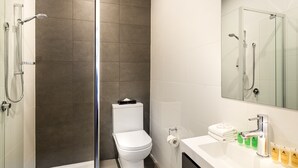 A modern bathroom with a glass-enclosed shower, a white toilet, and a vanity with toiletries. - Como Court (St Kilda)