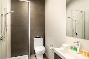 A modern bathroom with a glass-enclosed shower, a white toilet, and a vanity with toiletries. - Como Court (St Kilda)