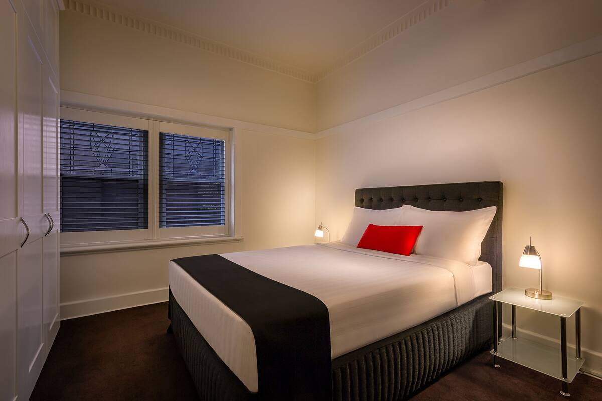 A neatly made bed with a black and white headboard, a red pillow, and two bedside lamps.