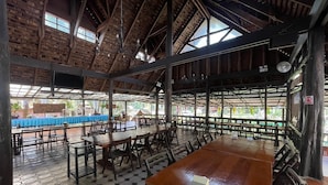 A spacious indoor area with high ceilings and wooden beams, featuring multiple tables and chairs arranged for dining.