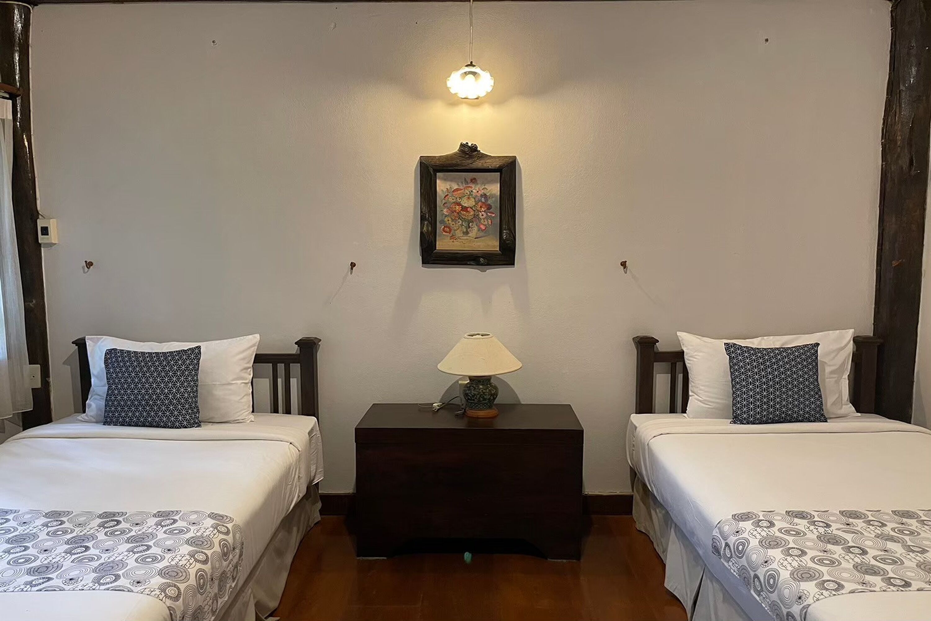 A bedroom with two beds, a nightstand with a lamp, and a framed picture on the wall.