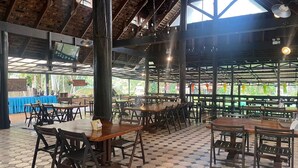 An indoor dining area with hexagonal patterned flooring, wooden tables and chairs, and a high ceiling with exposed beams.