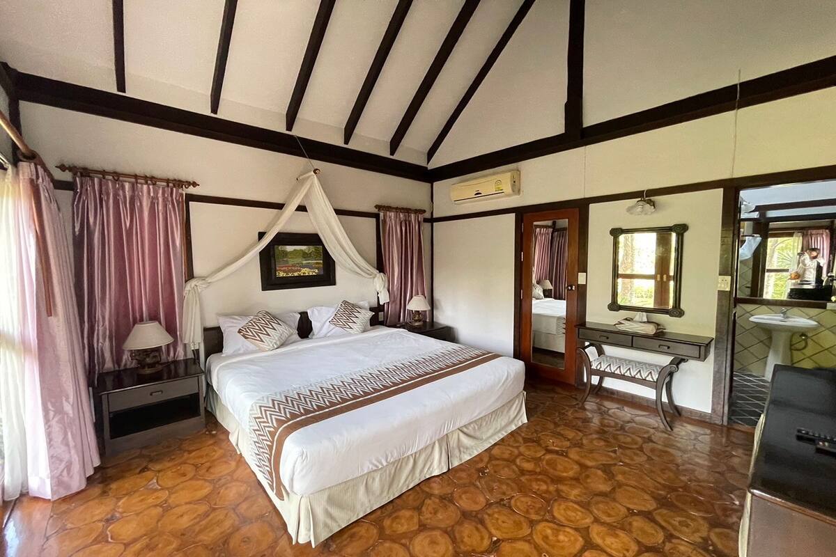 Un dormitorio con una cama grande, una mesita de noche, un tocador con espejo y un baño visible a través de una puerta abierta.