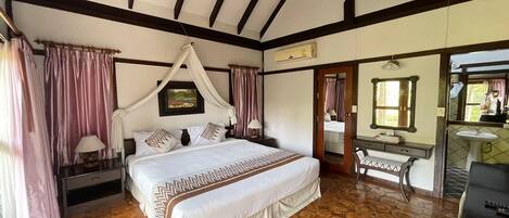 Un dormitorio con una cama grande, una mesita de noche, un tocador con espejo y un baño visible a través de una puerta abierta.