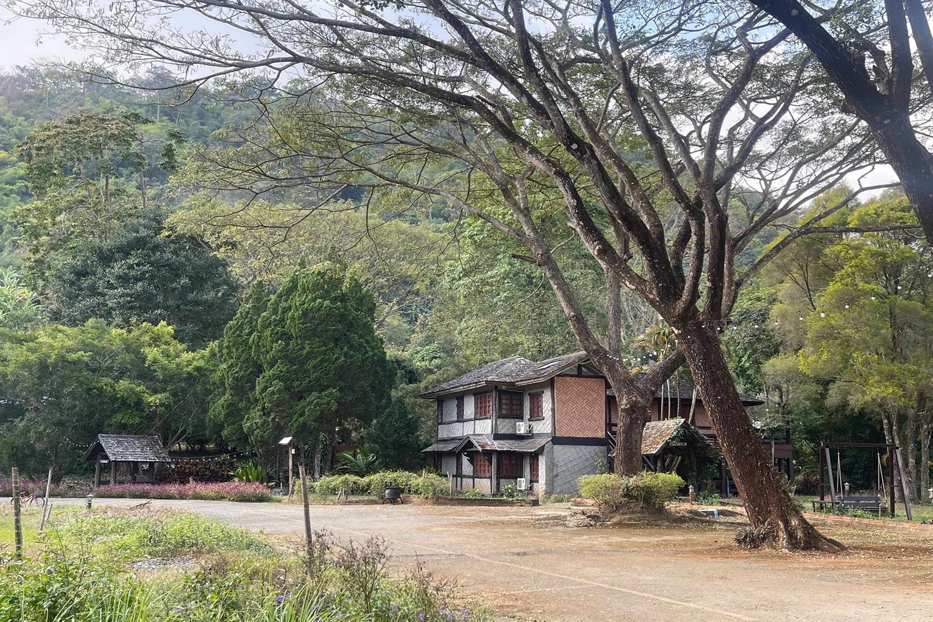 A traditional two-story house with a tiled roof, surrounded by lush greenery and trees.