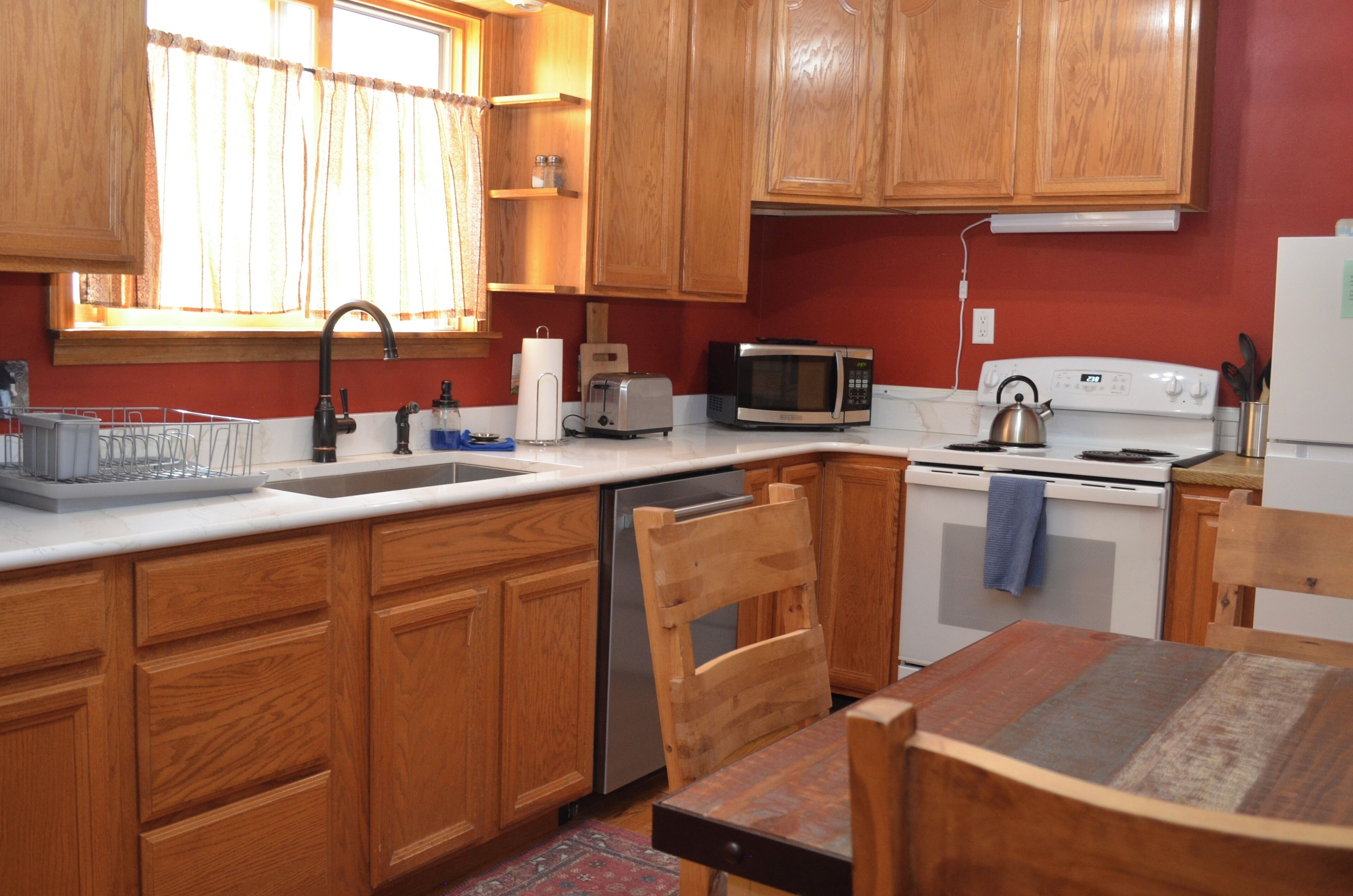 A kitchen with wooden cabinets, a white countertop, a sink, a microwave, a stove, and a dining table with chairs.