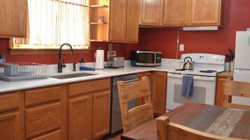 A kitchen with wooden cabinets, a white countertop, a sink, a microwave, a stove, and a dining table with chairs.