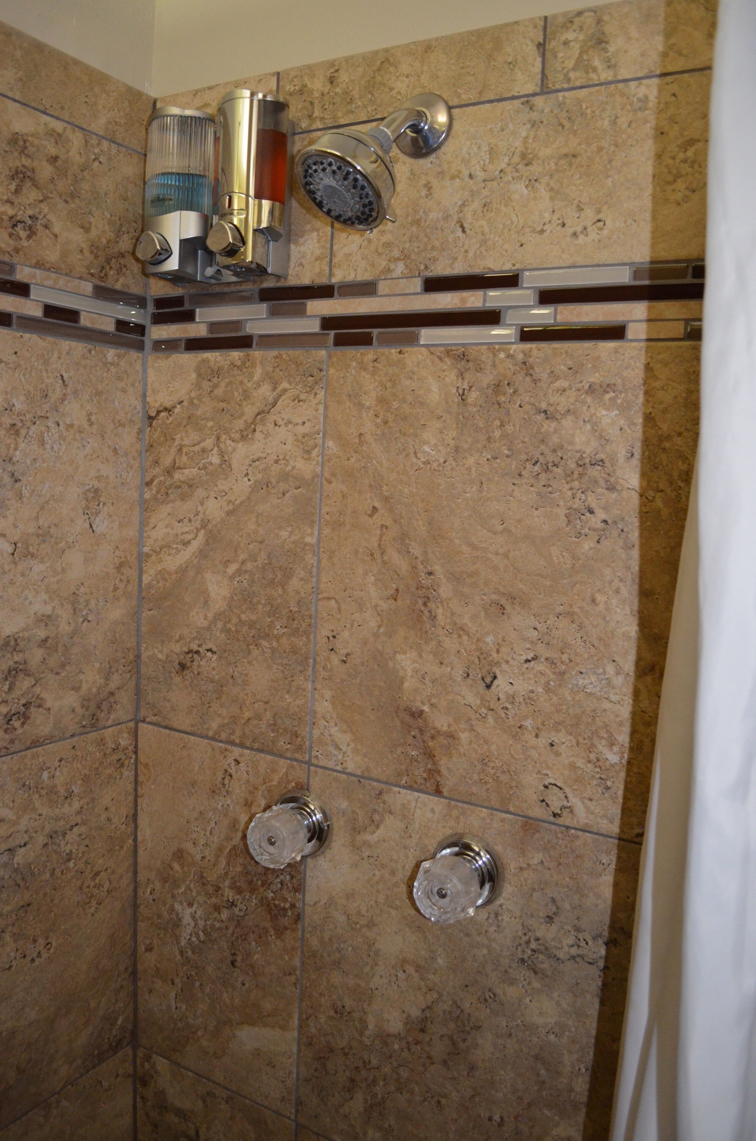 Ducha con puerta de vidrio, cabezal de ducha en la pared y suelo de baldosas.