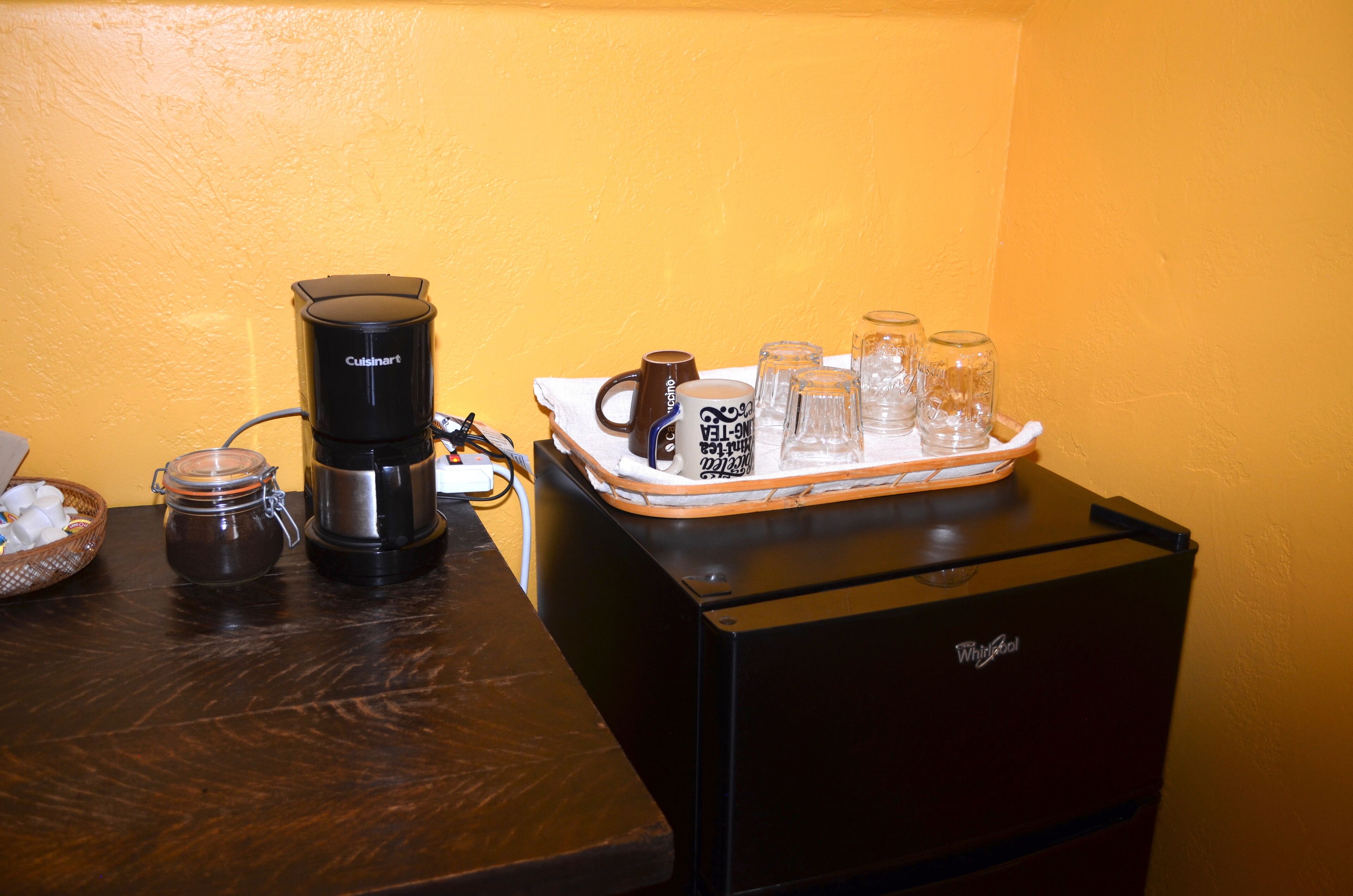 A kitchenette with a coffee maker, a tray with mugs and glasses, and a jar of sugar.