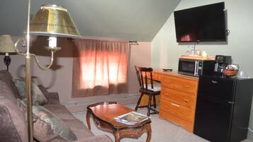 Un espacio habitable compacto con sofá, una mesa de centro de madera, televisión montada en la pared, microondas, refrigerador y cómoda de madera.