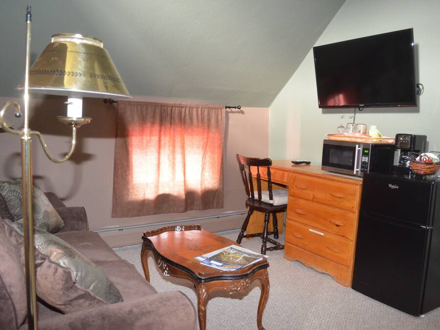 Un espacio habitable compacto con sofá, una mesa de centro de madera, televisión montada en la pared, microondas, refrigerador y cómoda de madera.