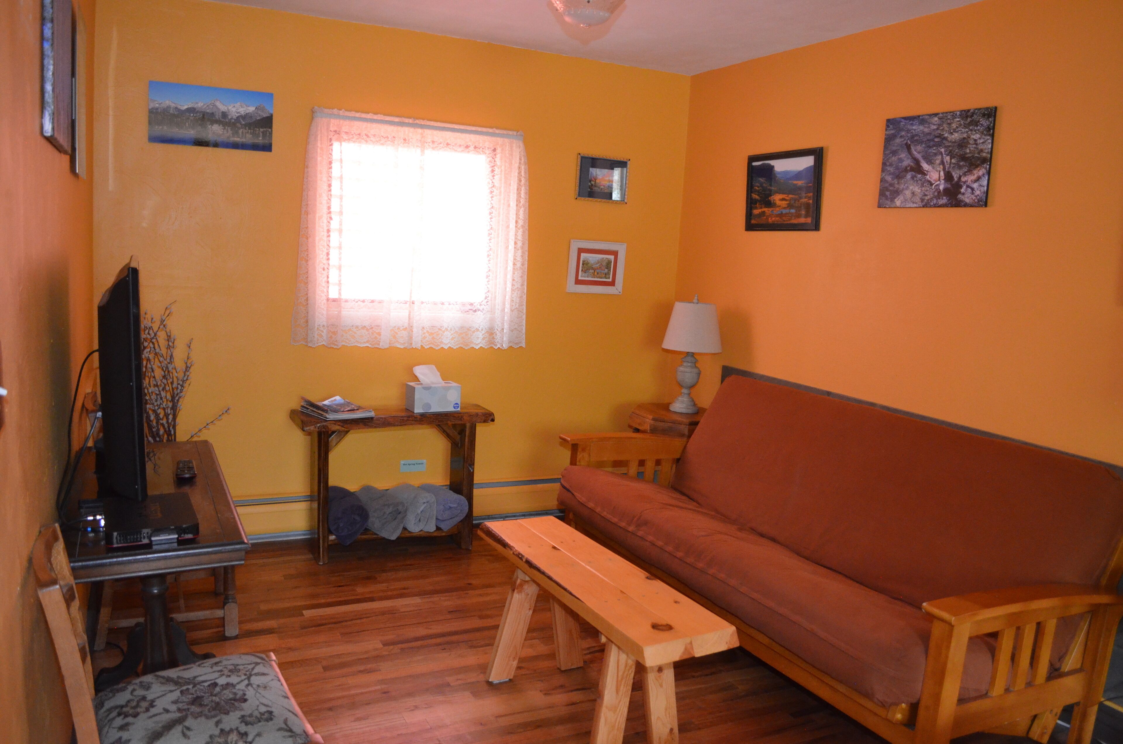 A living room with a wooden bench, a sofa, a television, and a window with lace curtains.
