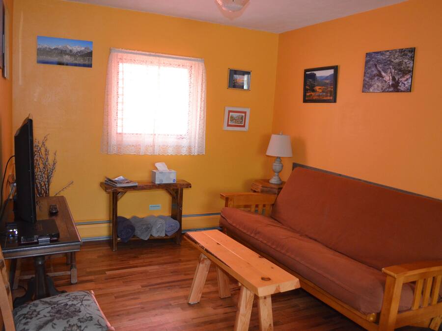 A living room with a wooden bench, a sofa, a television, and a window with lace curtains.