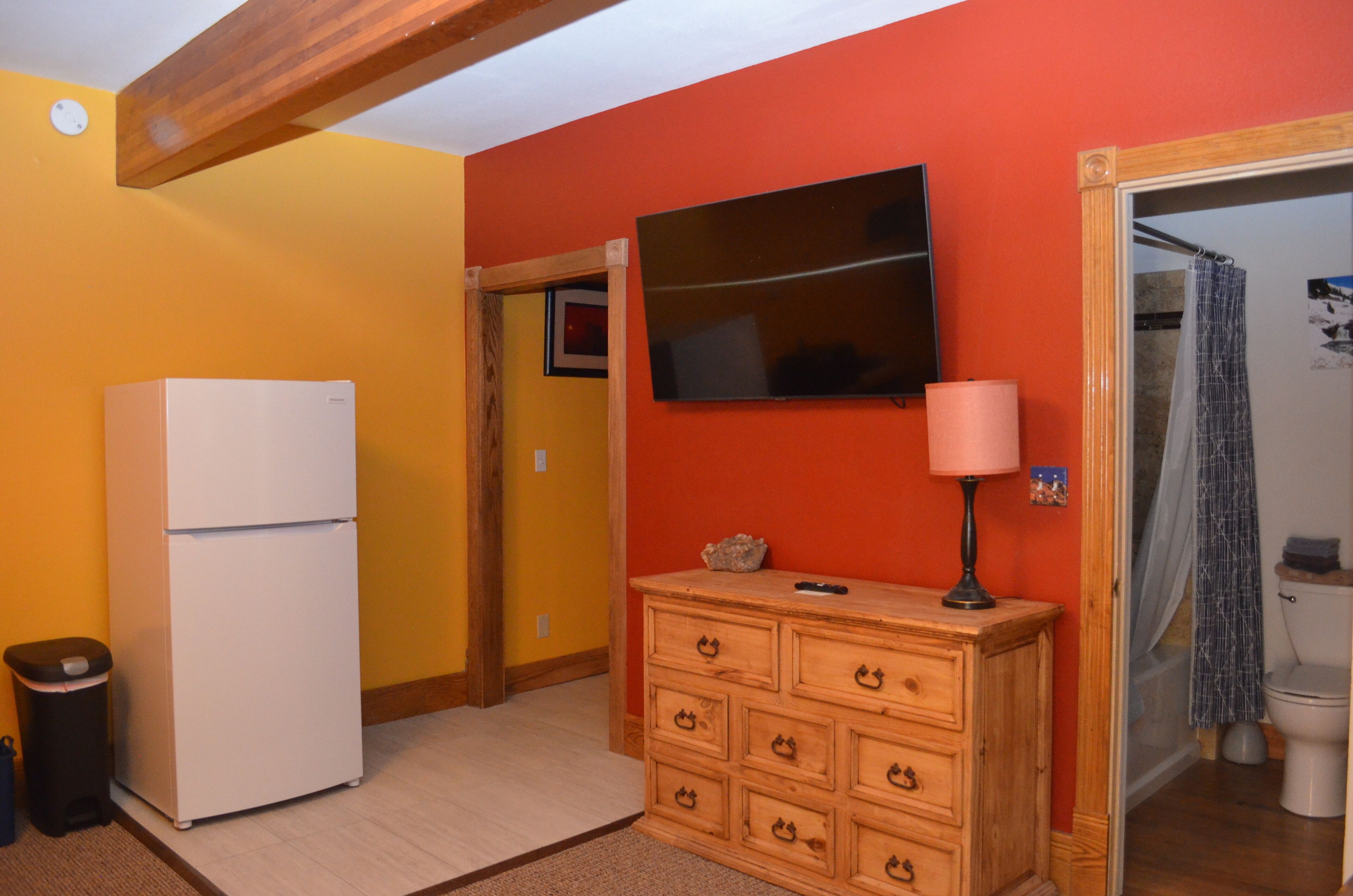 A compact kitchen with a refrigerator, wooden dresser, and a television on the wall.