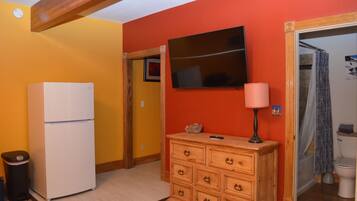 A compact kitchen with a refrigerator, wooden dresser, and a television on the wall.