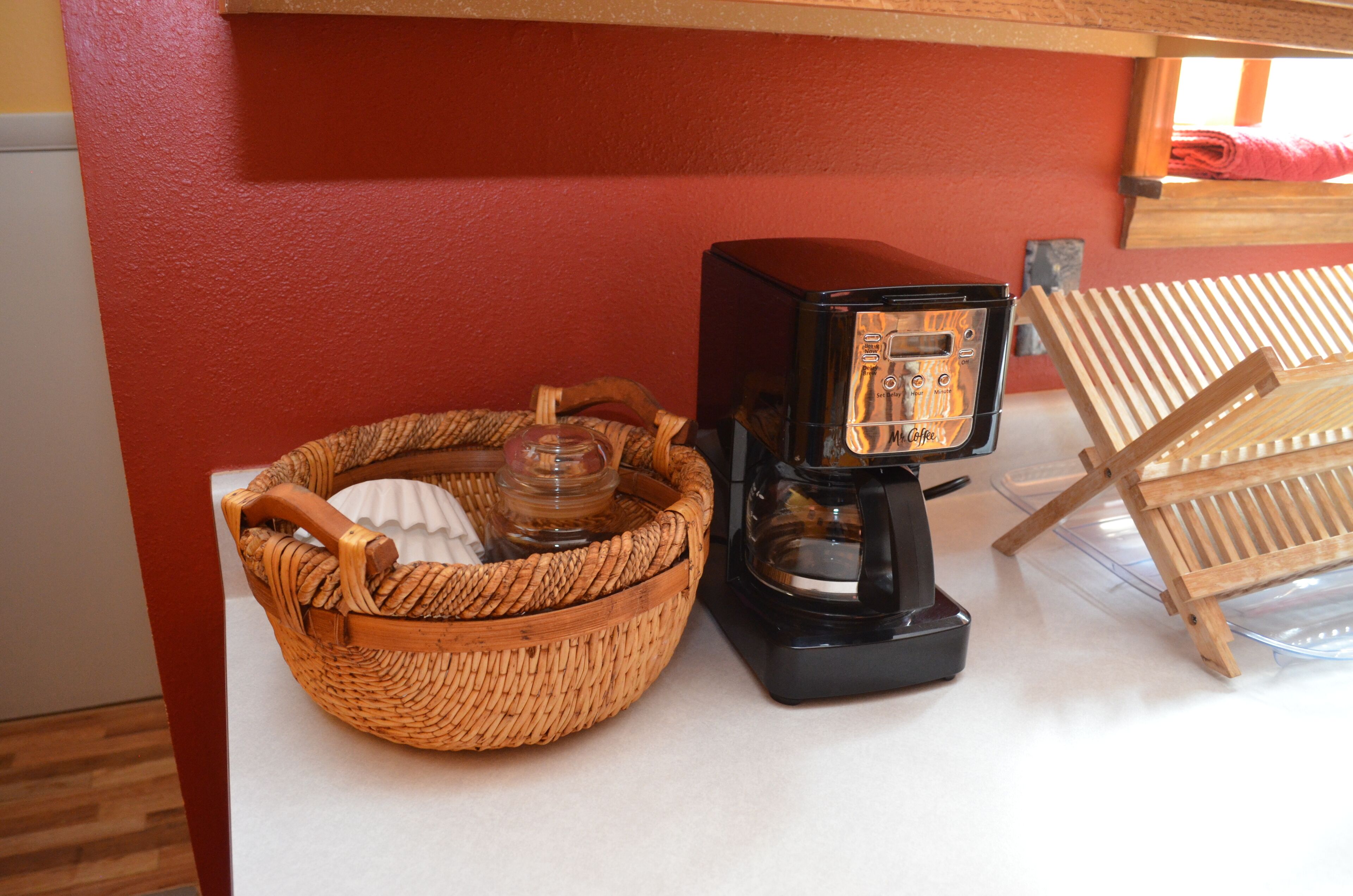 Une machine à café, un panier en osier et une chaise en bois, le tout placé devant un mur rouge.