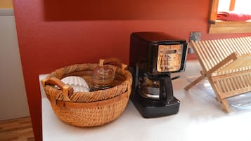 Une machine à café, un panier en osier et une chaise en bois, le tout placé devant un mur rouge.