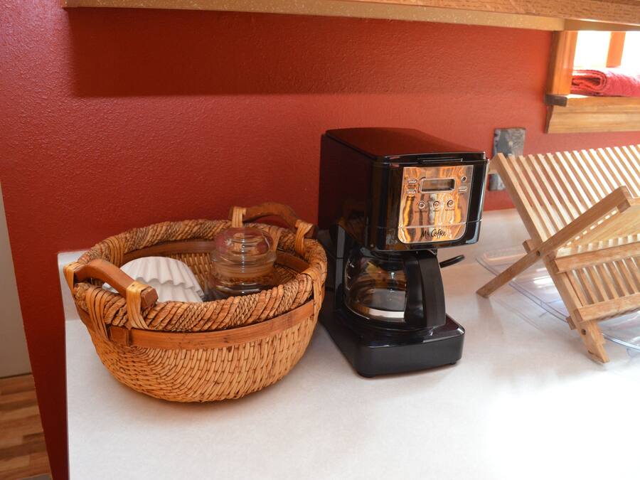 Une machine à café, un panier en osier et une chaise en bois, le tout placé devant un mur rouge.