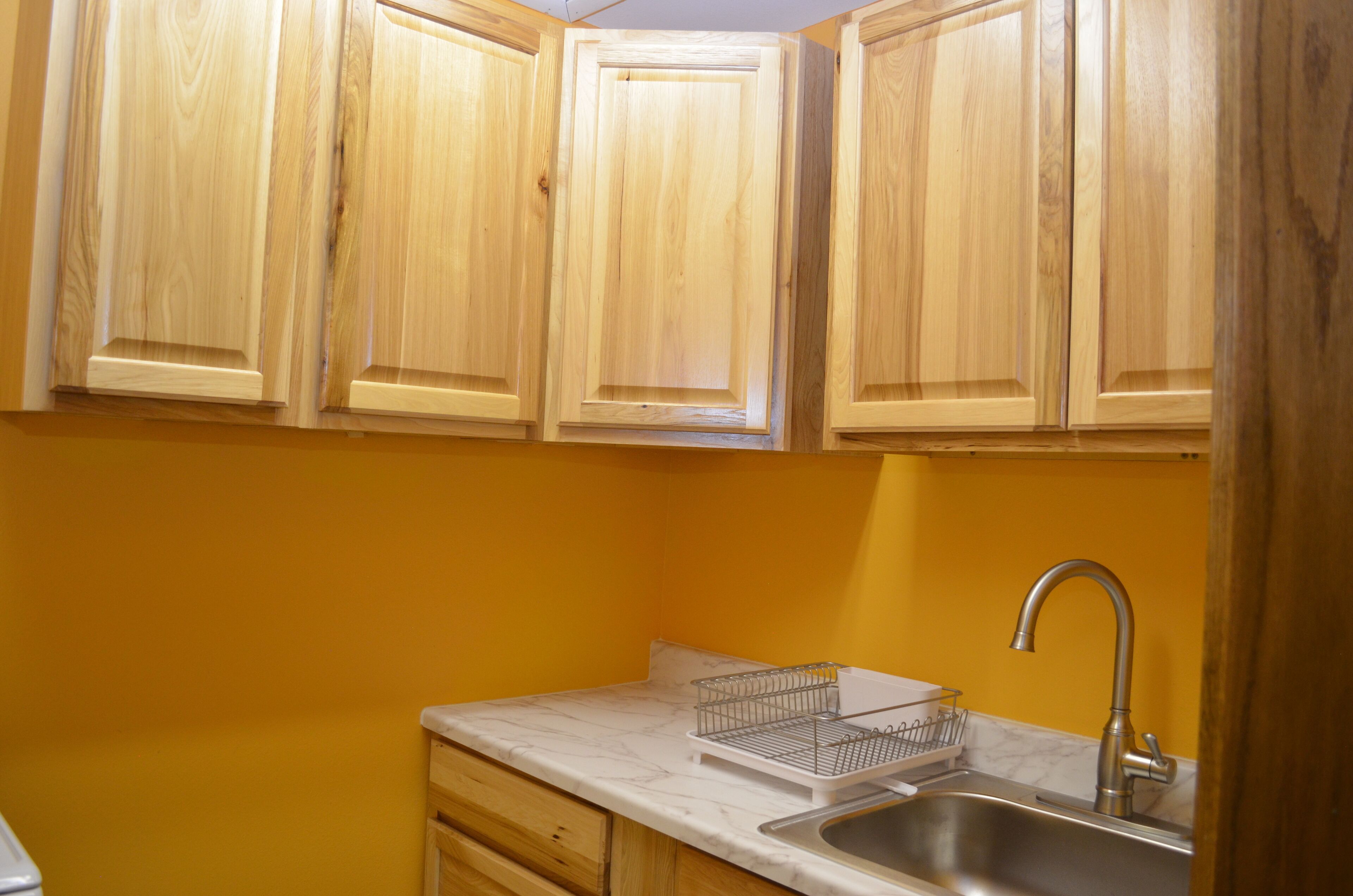 A kitchen with wooden cabinets, a white marble countertop, a stainless steel sink, and a wire basket.