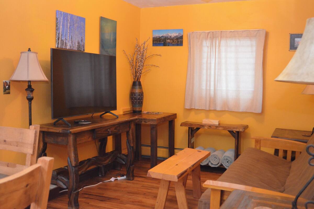 A cozy living room with wooden furniture, a flat-screen TV, and a vase with branches.