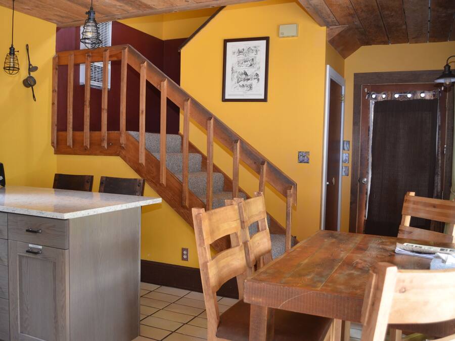 A kitchen with wooden cabinets, a dining table with chairs, a staircase, and a door with a curtain.
