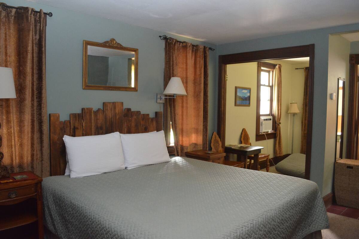 A hotel room with a large bed, wooden headboard, a mirror, a desk, and a chair.