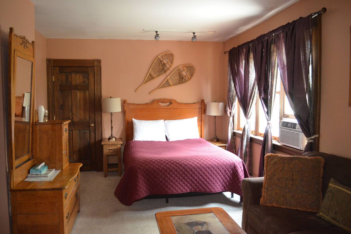 A bedroom with a wooden bed, a dresser, a chair, and a large mirror.