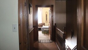 A narrow hallway with a wooden door at the end, leading to a bedroom with a bed and a nightstand. - Smedley's Suites (Silverton)