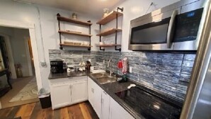 A modern kitchen with white cabinets, a black countertop, and a stainless steel microwave. - Smedley's Suites (Silverton)