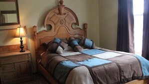 A bedroom with a wooden bed, a nightstand, a lamp, and a mirror on the wall. - Smedley's Suites (Silverton)