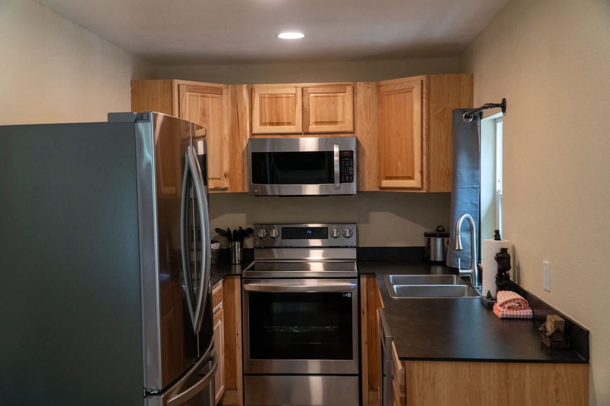 A modern kitchen with stainless steel appliances, wooden cabinets, and a black countertop.