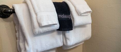 Una pila de toallas blancas en un toallero, con una toalla negra que tiene la palabra 'makeup' escrita.