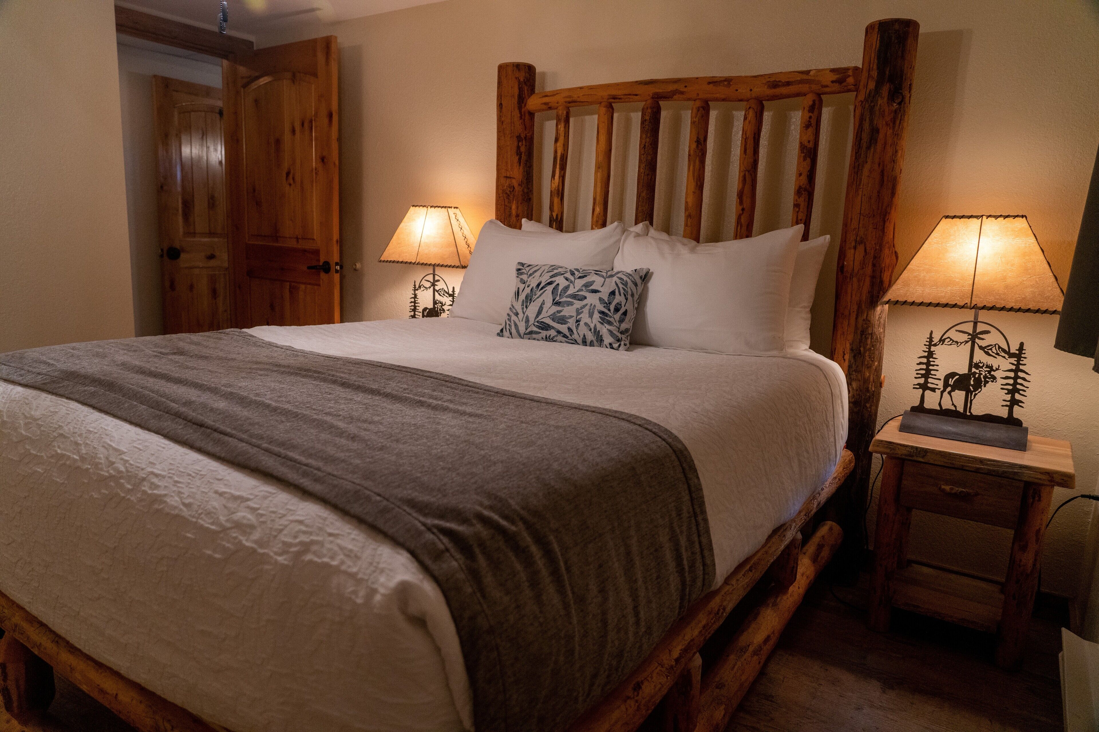 A bed with a wooden headboard, two bedside tables with lamps, and a door in the background.