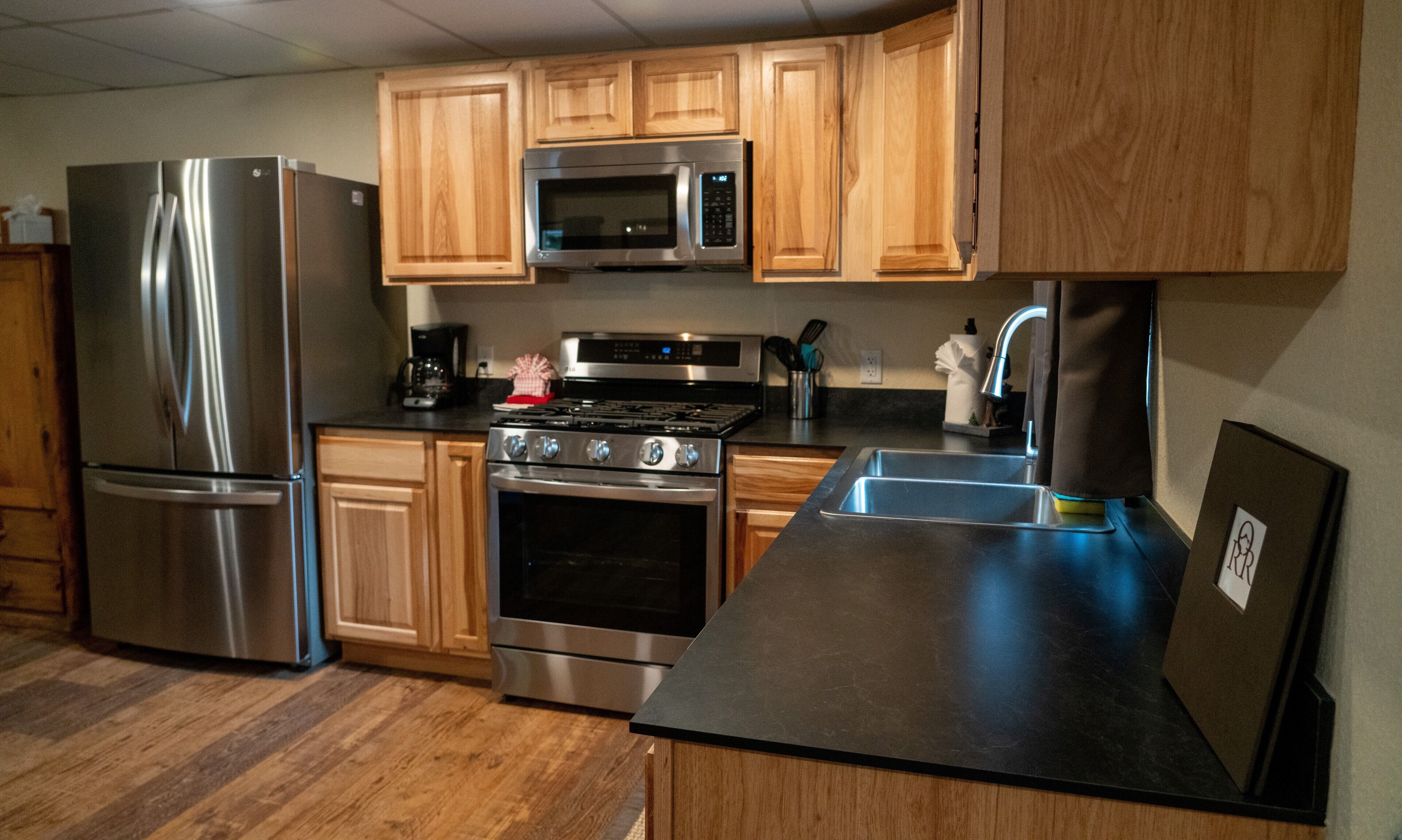 A modern kitchen with wooden cabinets, stainless steel appliances, and a black countertop.