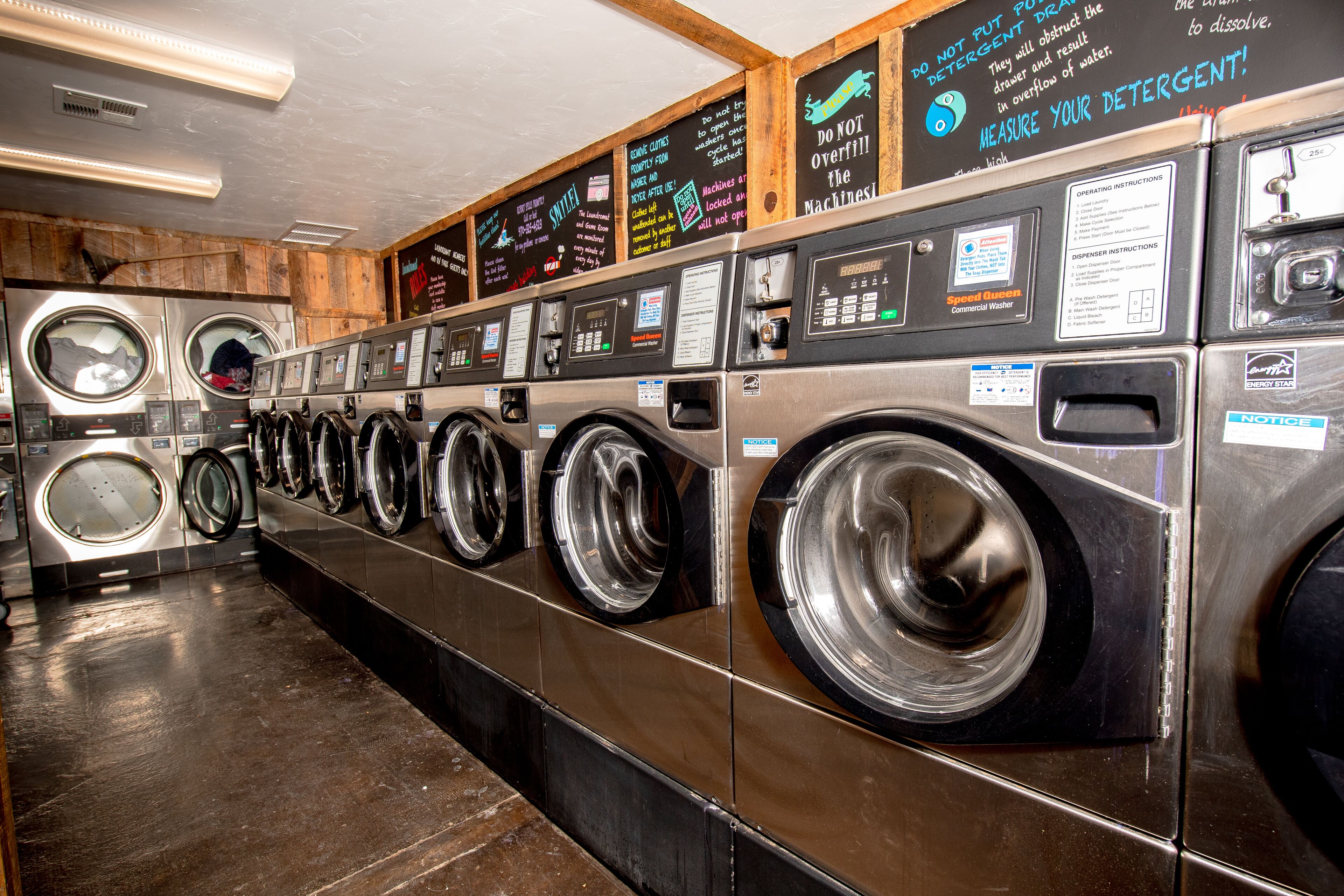 A row of commercial washers and dryers in a facility with instructional signs on the wall.
