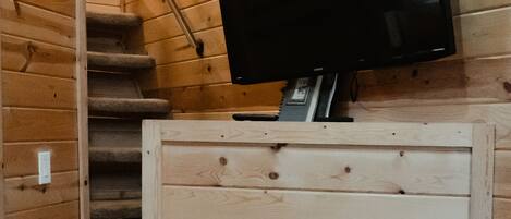 A wooden interior with a fireplace, a television mounted on the wall, and a staircase.